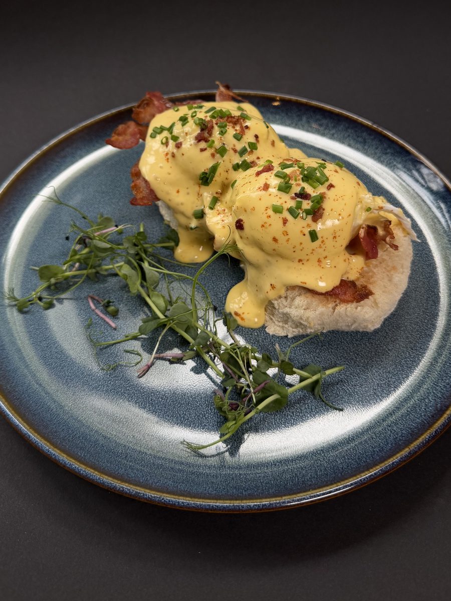 Eggs Benedict with hollandaise and micro herbs on a blue plate