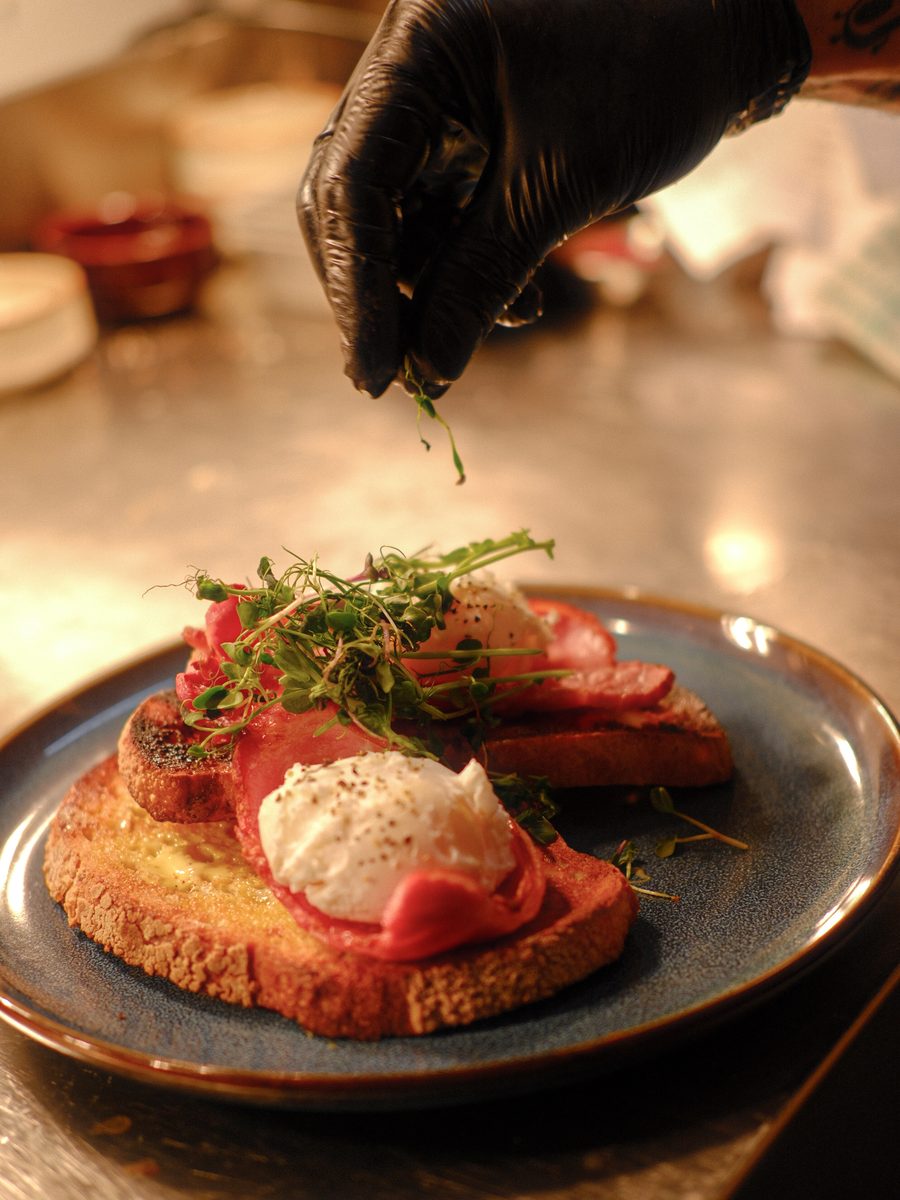 A chef adding herbs to a plate of eggs on sourdough at the pass